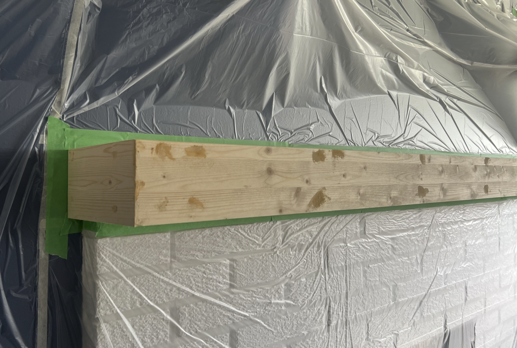Closeup of new wood mantel with wood filler applied and wall taped and hoarded off.