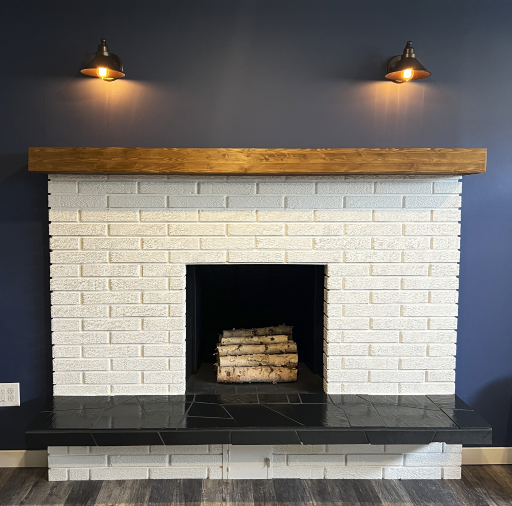 Refinished white painted brick fireplace with wood mantle and black tile hearth on a white wall